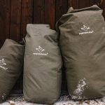 Three durable canvas camping bags from White Duck Outdoors resting against a wooden wall, designed for heavy-duty outdoor gear storage.