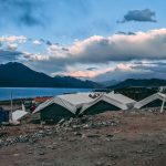 Disaster relief tents set up near a lake and mountains, providing emergency shelter for people in need.