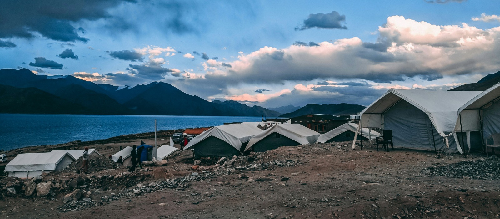 Disaster relief tents set up near a lake and mountains, providing emergency shelter for people in need.