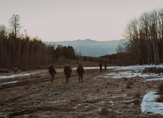 A group of people hiking together through a snowy field with trees and mountains in the distance, exploring the outdoors at sunset.
