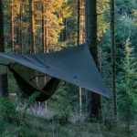 Camping hammock setup with a tarp shelter in a forest for outdoor protection and shade