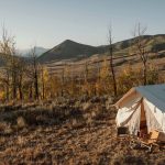 A canvas wall tent set up in the mountains surrounded by fall trees and scenic views, perfect for camping in nature.