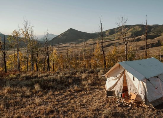 A canvas wall tent set up in the mountains surrounded by fall trees and scenic views, perfect for camping in nature.