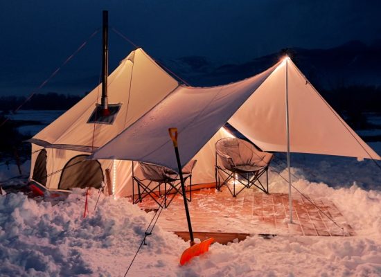 A warm canvas tent with a wood stove glowing at night, surrounded by snow and mountain views.