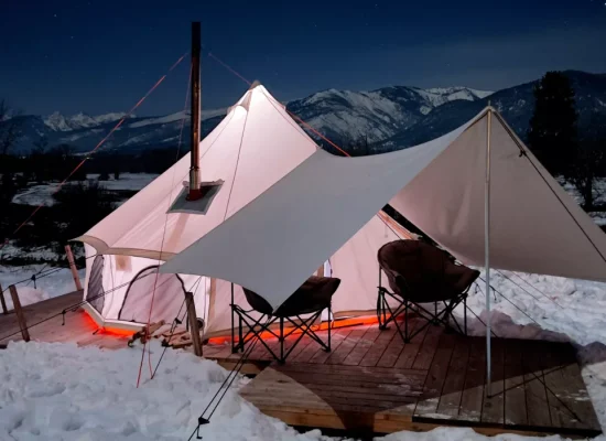 Insulated yurt tent with a stove and tarp in a snowy mountain landscape for cozy winter camping.