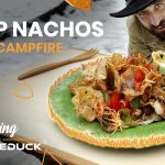 Jack Steward enjoying cheesy campfire nachos cooked outdoors, part of the Wandering with WhiteDuck series on outdoor cooking.