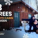 Couple sitting with their dog in deep snow outside a remote wooden cabin in the woods during extreme winter temperatures of minus 33 degrees.