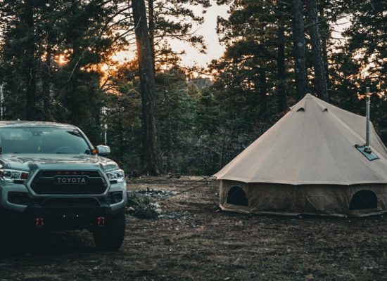 Toyota pickup truck parked beside a canvas bell tent in a forest campsite at sunset.