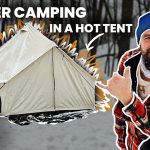 Man in winter gear beside a canvas tent during snowy camping with White Duck Outdoors logo.