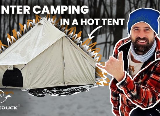 Man in winter gear beside a canvas tent during snowy camping with White Duck Outdoors logo.