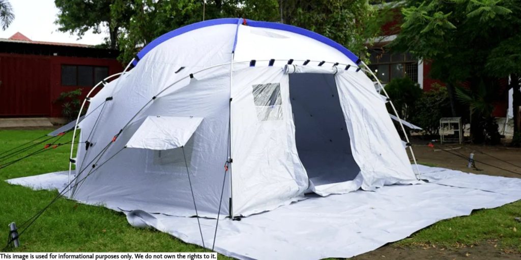 Exterior side view of a white geodesic tent featuring multiple guy lines, a small side window flap, and a large open doorway.