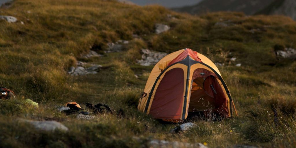 Orange and red lightweight backpacking tent pitched on a rocky mountain ridge during golden hour.