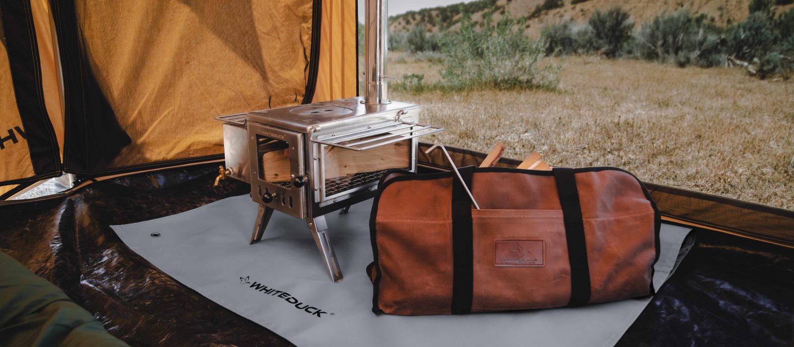 Tent stove set up inside a canvas tent with a fireproof mat and carry bag, providing safe and efficient heating for camping