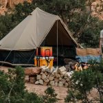 Canvas tent campsite setup with campfire, outdoor kitchen, and gear for comfortable camping without an RV in a desert landscape.