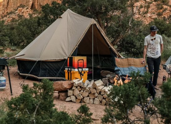 Canvas tent campsite setup with campfire, outdoor kitchen, and gear for comfortable camping without an RV in a desert landscape.