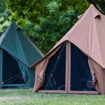 Canvas tents secured with properly angled guylines, demonstrating improved tent stability and wind resistance in outdoor camping conditions.