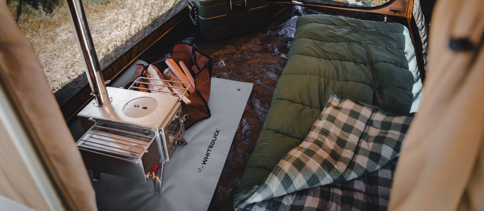 Sleeping bag laid out inside a canvas camping tent with a wood stove and camping gear for a warm and comfortable outdoor setup