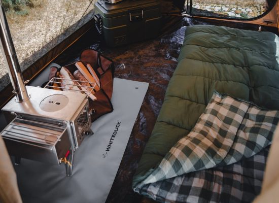 Sleeping bag laid out inside a canvas camping tent with a wood stove and camping gear for a warm and comfortable outdoor setup