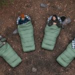 Group of campers lying outdoors in green sleeping bags, demonstrating sleeping bag temperature ratings for cold-weather camping
