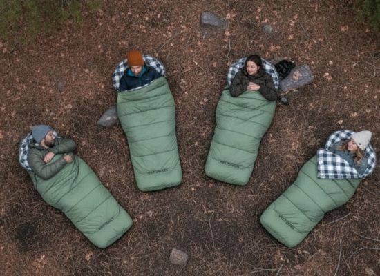 Group of campers lying outdoors in green sleeping bags, demonstrating sleeping bag temperature ratings for cold-weather camping