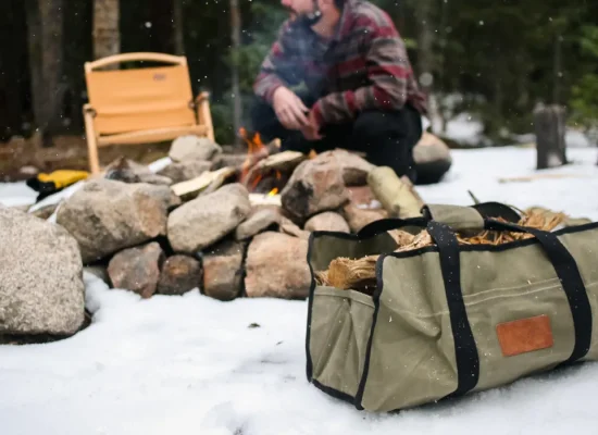 Canvas firewood carrier filled with logs at a snowy campsite.