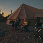 Family camping together by a campfire, relaxing outside a large tent during an evening outdoor trip.