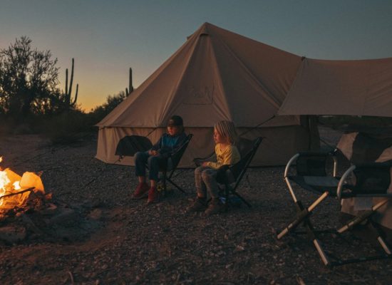 Family camping together by a campfire, relaxing outside a large tent during an evening outdoor trip.