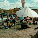 People sitting near tents at an outdoor camping basecamp during a festival