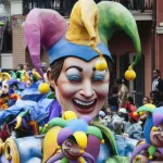 Mardi Gras parade float with colorful jester masks and crowd in New Orleans
