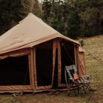 Wind-resistant canvas tent securely staked with guylines, set up for camping in high winds at a forest campsite.