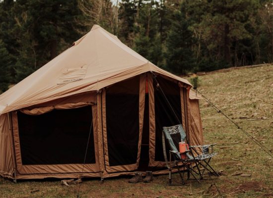 Wind-resistant canvas tent securely staked with guylines, set up for camping in high winds at a forest campsite.