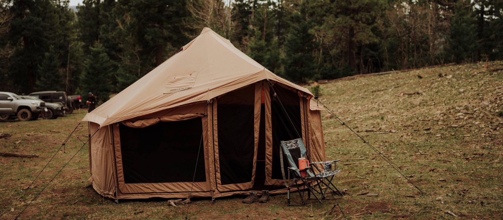 Wind-resistant canvas tent securely staked with guylines, set up for camping in high winds at a forest campsite.