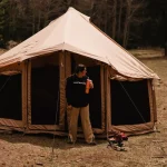 Camper standing outside a durable canvas tent in a forest, highlighting high quality camping gear choice