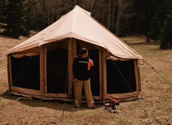 Camper standing outside a durable canvas tent in a forest, highlighting high quality camping gear choice