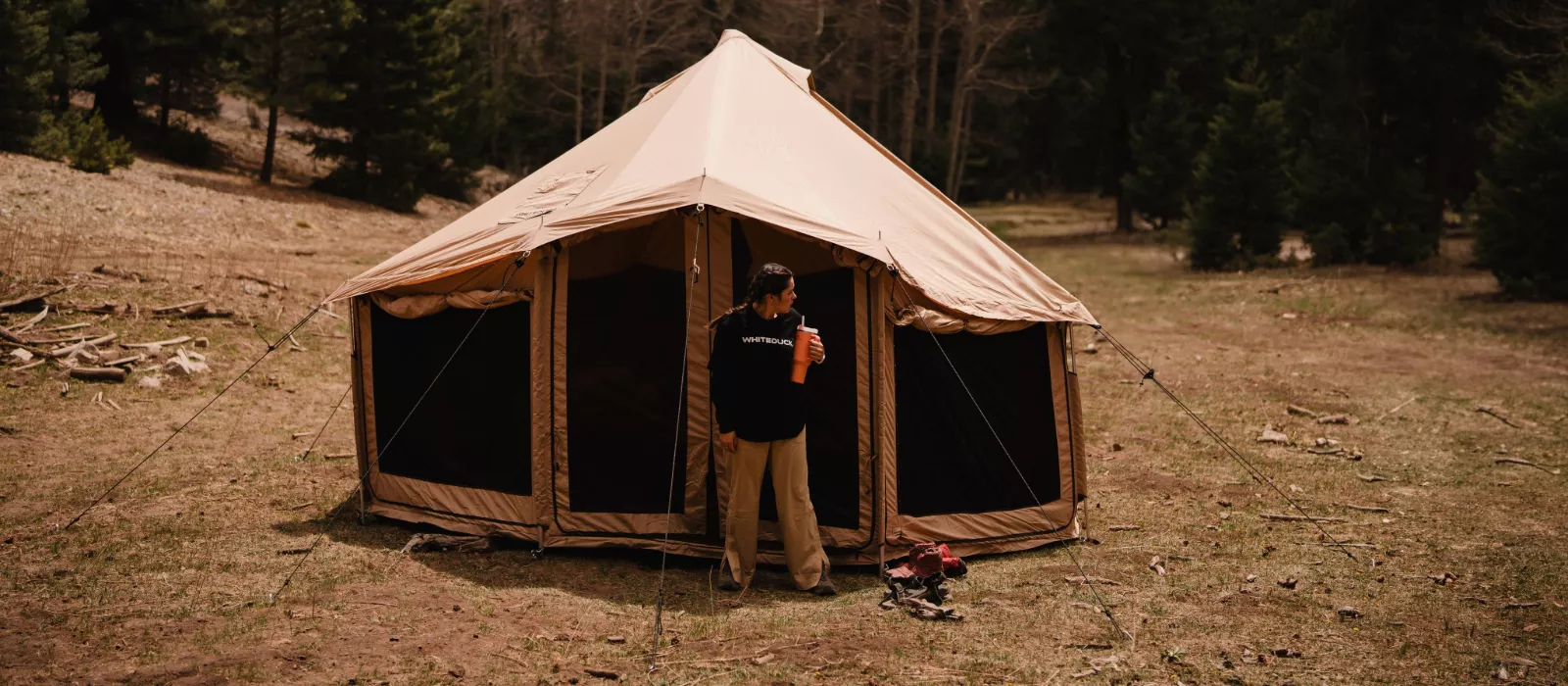 Camper standing outside a durable canvas tent in a forest, highlighting high quality camping gear choice