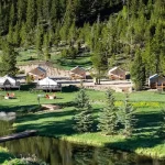 Glamping tents set along a lakeside forest campsite with green landscape, trees, and peaceful outdoor surroundings.
