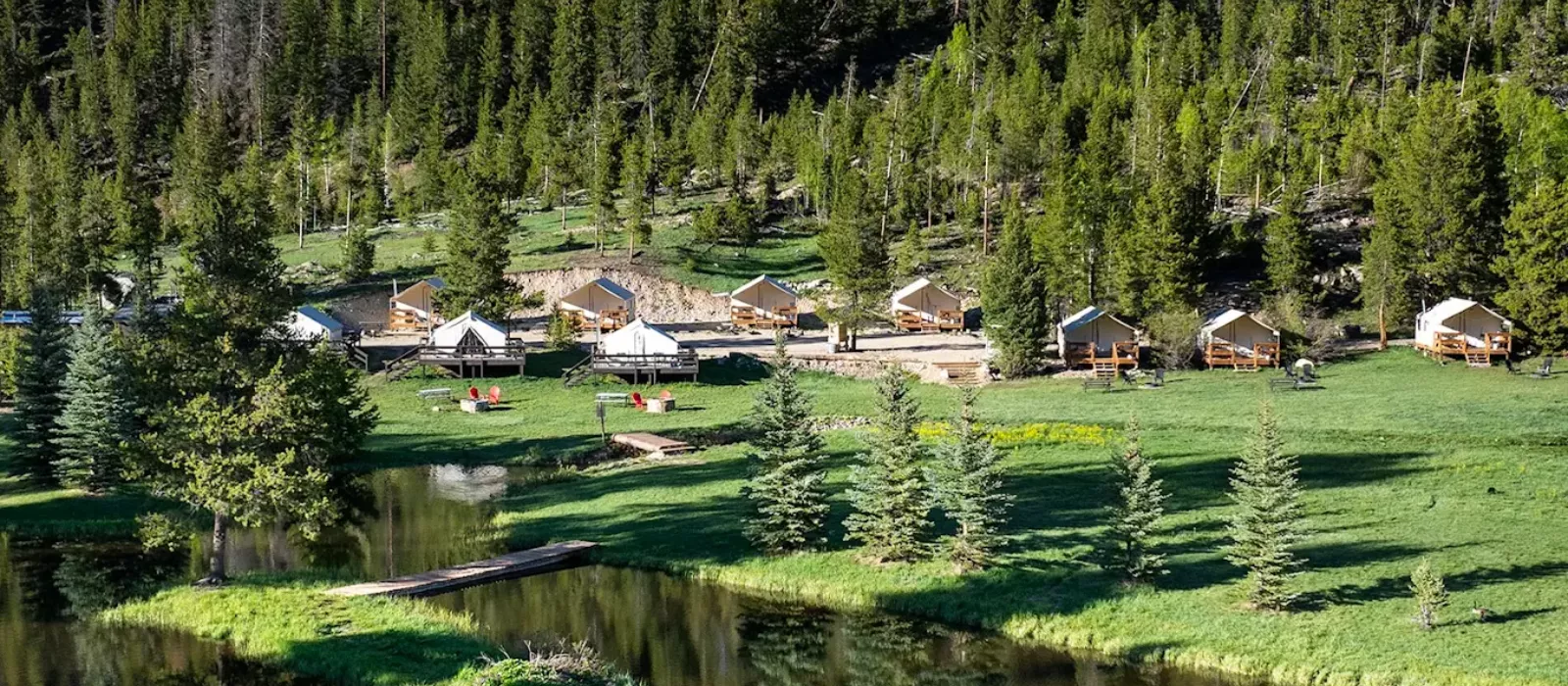 Glamping tents set along a lakeside forest campsite with green landscape, trees, and peaceful outdoor surroundings.