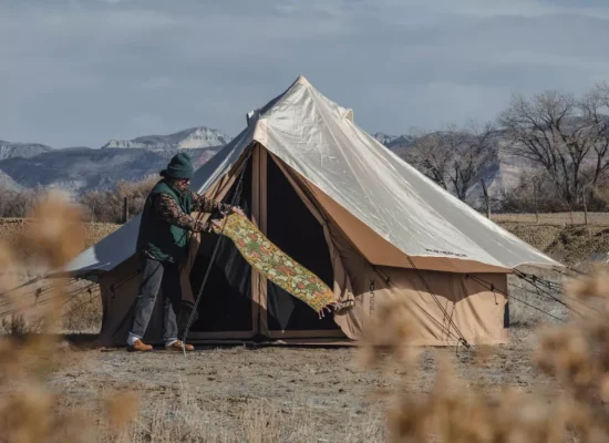 A spacious canvas tent set up for glamping in a scenic canyon landscape with mountains in the background and a cozy outdoor seating area.