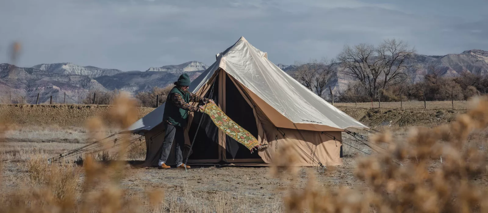 A spacious canvas tent set up for glamping in a scenic canyon landscape with mountains in the background and a cozy outdoor seating area.