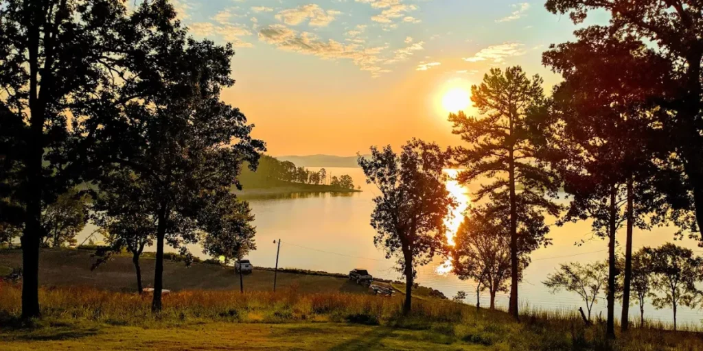 Golden hour sunset over Lake Broken Bow, Oklahoma, with trees silhouetted and calm water.
Credit: Lake Broken Bow GMB
