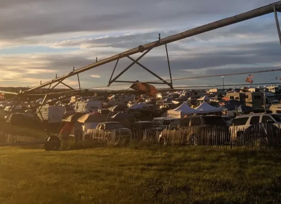 Large campsite at the Gorge during sunset with tents, vehicles, and a long irrigation structure overlooking a crowded camping area.