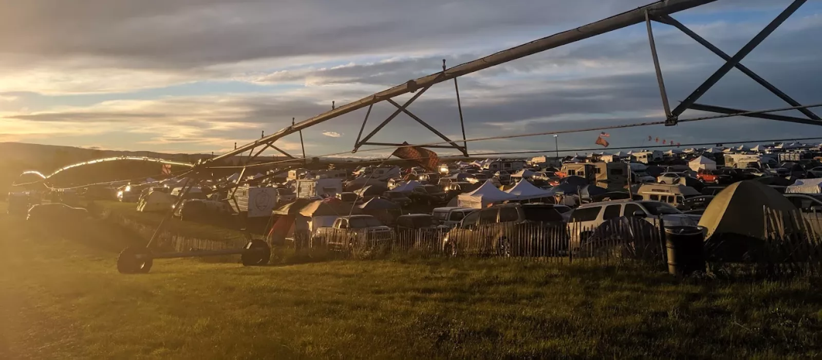 Large campsite at the Gorge during sunset with tents, vehicles, and a long irrigation structure overlooking a crowded camping area.