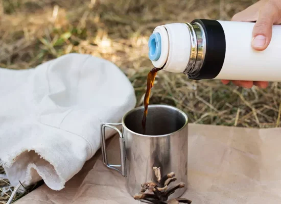 Cowboy coffee being poured from a thermos into a metal mug while camping outdoors