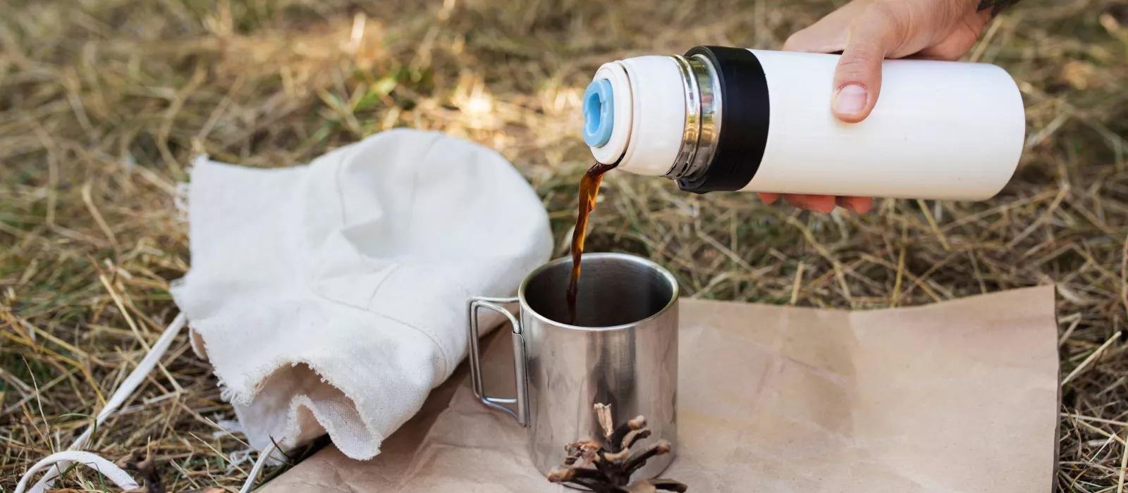 Cowboy coffee being poured from a thermos into a metal mug while camping outdoors