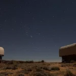 Two covered wagon-style glamping tents under a star-filled night sky in the Arizona desert landscape.
