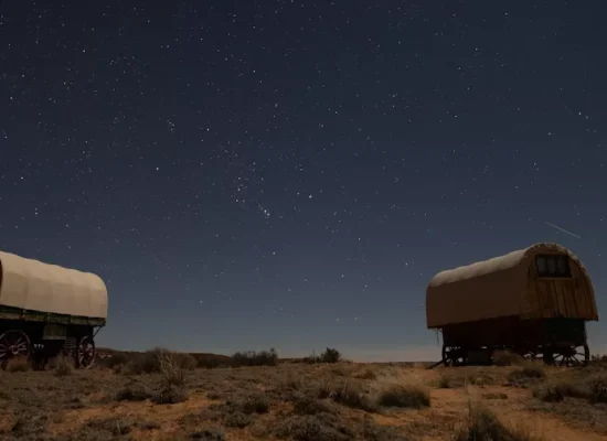 Two covered wagon-style glamping tents under a star-filled night sky in the Arizona desert landscape.