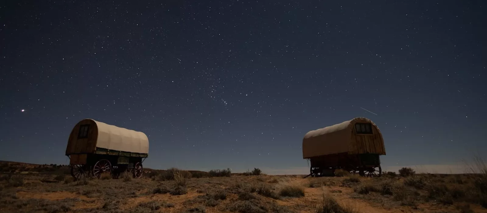 Two covered wagon-style glamping tents under a star-filled night sky in the Arizona desert landscape.