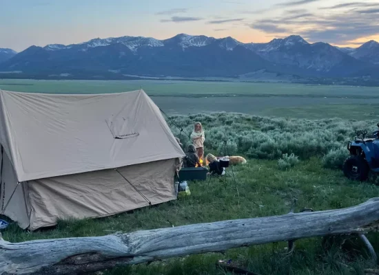 Multi-generational family camping with canvas tent and campfire in scenic mountain landscape