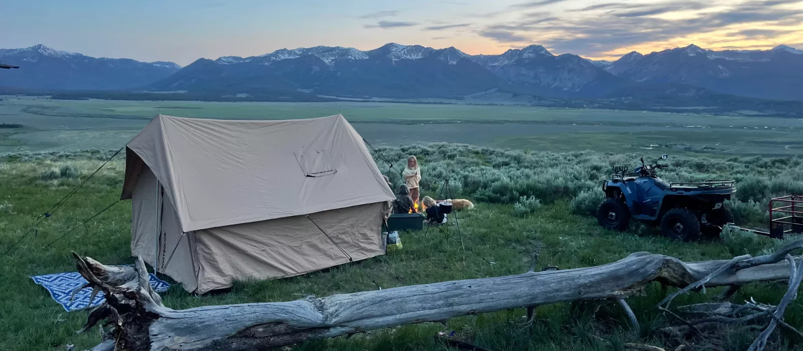 Multi-generational family camping with canvas tent and campfire in scenic mountain landscape