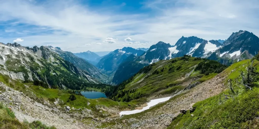 Panoramic view of alpine mountains and lake near Sahale Glacier with green valleys and rugged peaks. Credit: Sahale Glacier Campground GMB